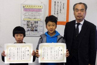 賞状を持つ二人の男の子と先生の写真