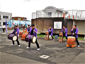紫色のはっぴを着て和太鼓を叩く学生たちの写真